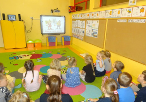 Grupa dzieci siedzi przed tablicą interaktywną i ogląda prezentację multimedialną na temat praw dziecka.